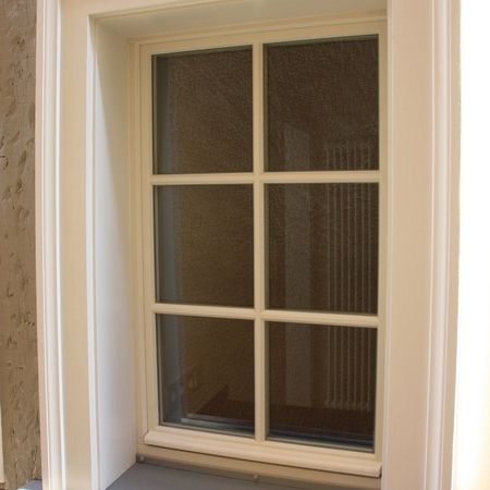 Innenansicht eines weißen Holzfensters mit klassischer Sprossenteilung, umgeben von einem schlichten Laibungsrahmen.
