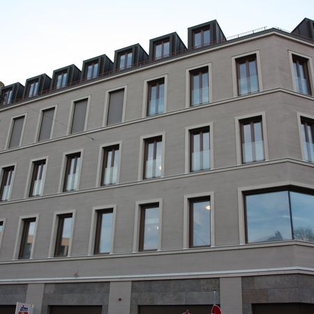 Seitenansicht des gleichen Gebäudes mit großen Fenstern und leicht abgeschrägter Ecke, im Erdgeschoss ein Geschäft.