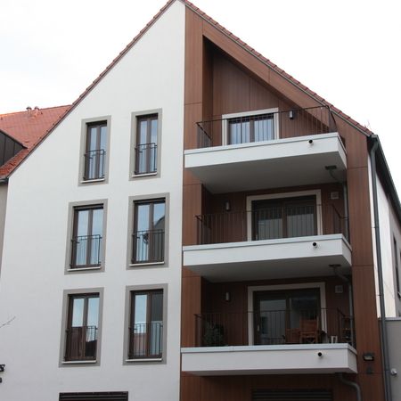 Modernes Mehrfamilienhaus mit weißen Balkonen, bodentiefen Fenstern und Holzfassade auf einer Gebäudeseite.