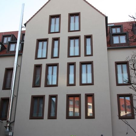 Hochgezogene Giebelfassade mit unterschiedlichen Fensterformaten, darunter zwei Reihen rechteckiger Fenster.