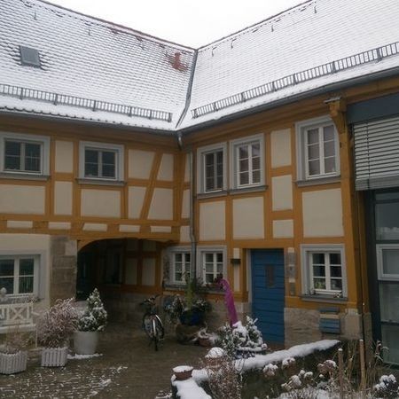 Fachwerkhaus mit gelber Fassade und Innenhof im Winter, Schnee bedeckt das Dach und den Boden.
