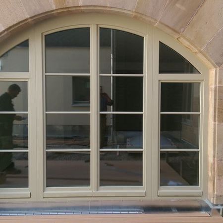Großes Segmentbogenfenster mit weißen Sprossen und vier Glasflächen, eingebaut in Natursteinfassade.