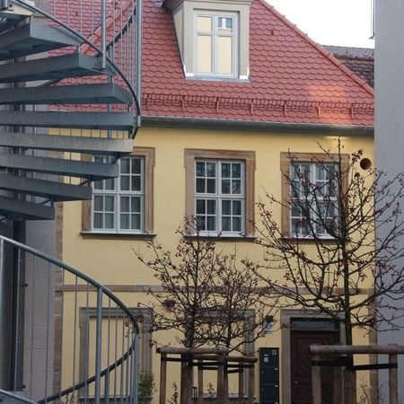 Gelbes Mehrfamilienhaus mit symmetrisch angeordneten weißen Sprossenfenstern und Natursteinrahmen.