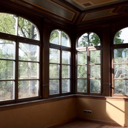 Innenansicht eines Raumes mit geöffnetem rundbogigem Holzfenster und detaillierter, dunkelbrauner Fensterverkleidung.