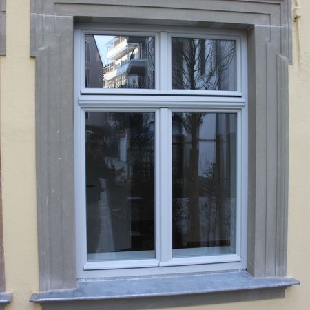 Nahaufnahme eines weißen Fensters mit Sprosseneinteilung in einem beigen Mauerrahmen.