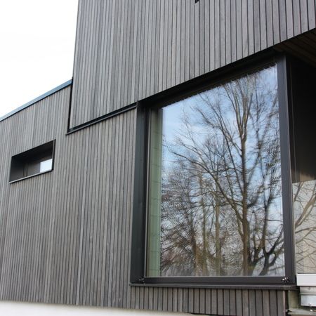 Großes bodentiefes Fenster mit Reflexion: Nahaufnahme eines großen Fensters mit dunklem Rahmen, das Bäume und Himmel spiegelt.