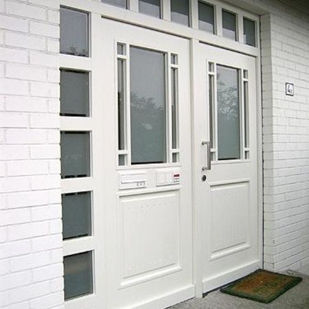 Weiße Haustür mit Glaseinsätzen: Zweiflügelige, weiße Haustür mit satinierten Glaselementen im Jugendstil, flankiert von schmalen Fensterfeldern, in weißer Klinkerfassade eingebaut.