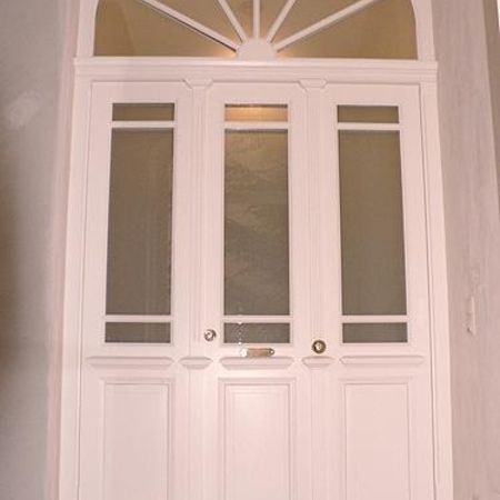 Weiße Hauseingangstür mit Oberlicht: Stilvolle, weiße Haustür mit drei länglichen Glaseinsätzen und Oberlicht in Sonnenstrahlen-Form, in hellem Innenbereich eingebaut.