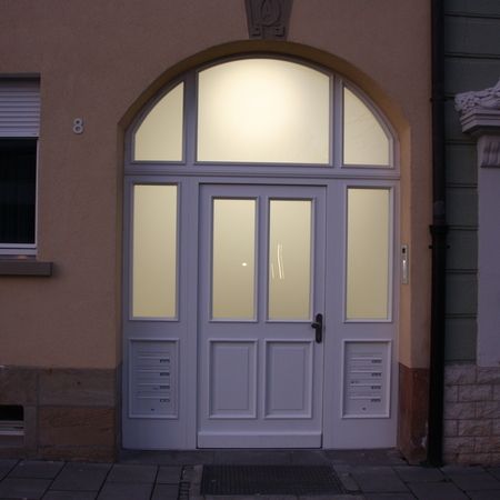 Weiße Hauseingangstür mit Rundbogen: Haustür mit Rundbogen und vier Glaseinsätzen, flankiert von Gegensprechanlage und Briefkästen, in Altbaufassade eingebaut.