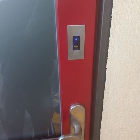 Fingerabdruckscanner mit LED-Anzeige oberhalb eines Türgriffs, montiert in eine rote Haustür mit Glaseinsatz.