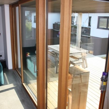 Innenansicht einer mehrteiligen Hebeschiebetür mit Holzrahmen und großen Glasflächen, die zur Terrasse mit Holzboden führt.