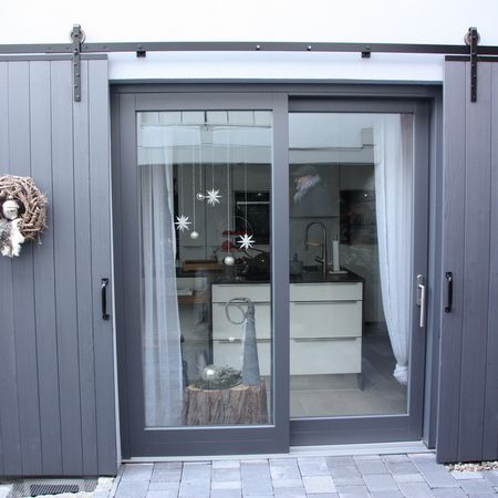 Hebeschiebetür aus grauem Aluminium mit symmetrischen Glasscheiben, seitlich eingefasst von dekorativen Holzschiebeläden.